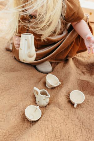 White ceramic teapot and cups arranged on a textured beige surface in a minimalist tea setting.