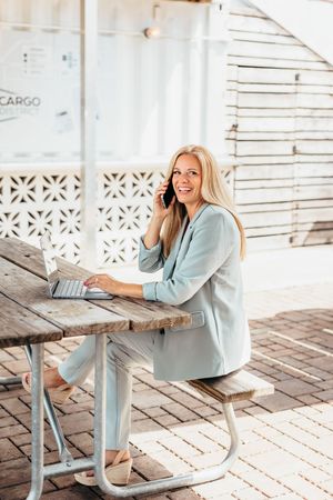Business woman in pale blue suit works on laptop in bright outdoor setting.