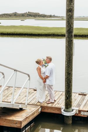 A couple shares a romantic moment together on a wooden dock overlooking a serene coastal marsh landscape.