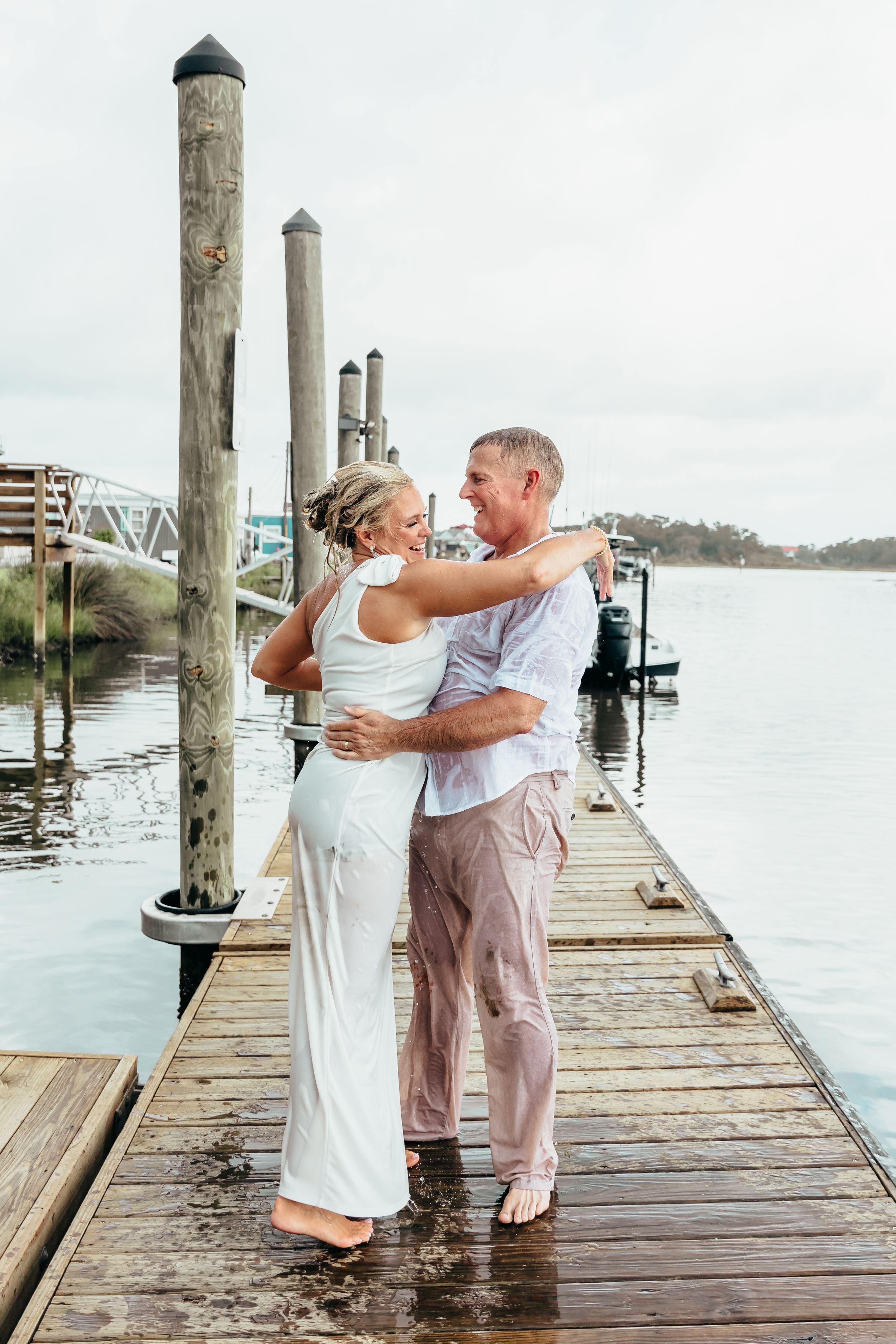 A couple shares a romantic moment after jumping into the water together on their elopement day. standing on a dock on an overcast day NC.