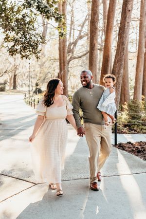 Family walking together on a sunlit path through tall pine trees on a beautiful day.