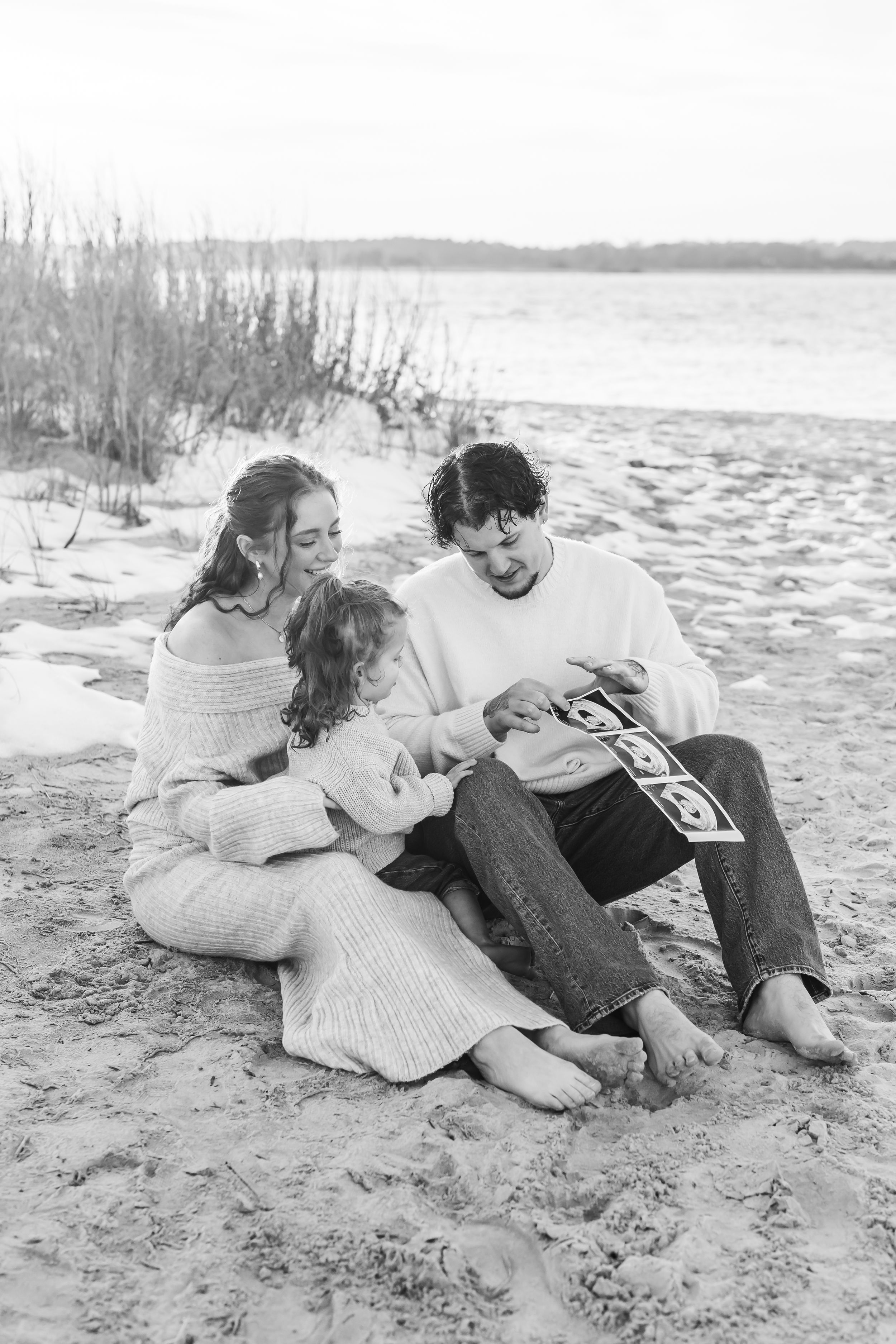 Black and white portrait of a family sitting together on a sandy beach.
