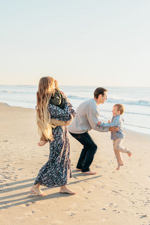 A family plays together on a sunny beach during golden hour, casting long shadows in the sand.