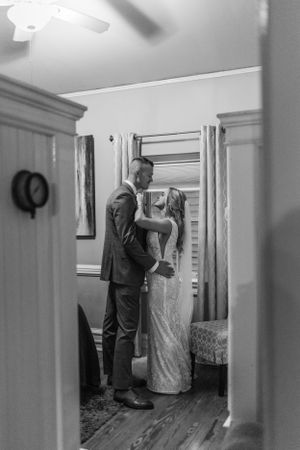 Black and white candid moment of wedding preparations through a doorway.