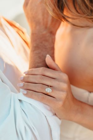Close up of a sparkling diamond engagement ring on a hand against soft white fabric.