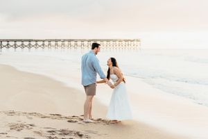 Couple takes romantic beach engagement photos during golden hour with pier in background.