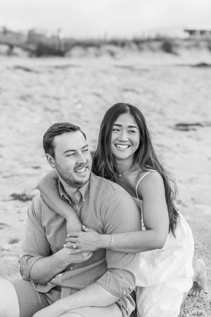 Black and white beach photos capture candid laughing moments between couple on sandy shore.