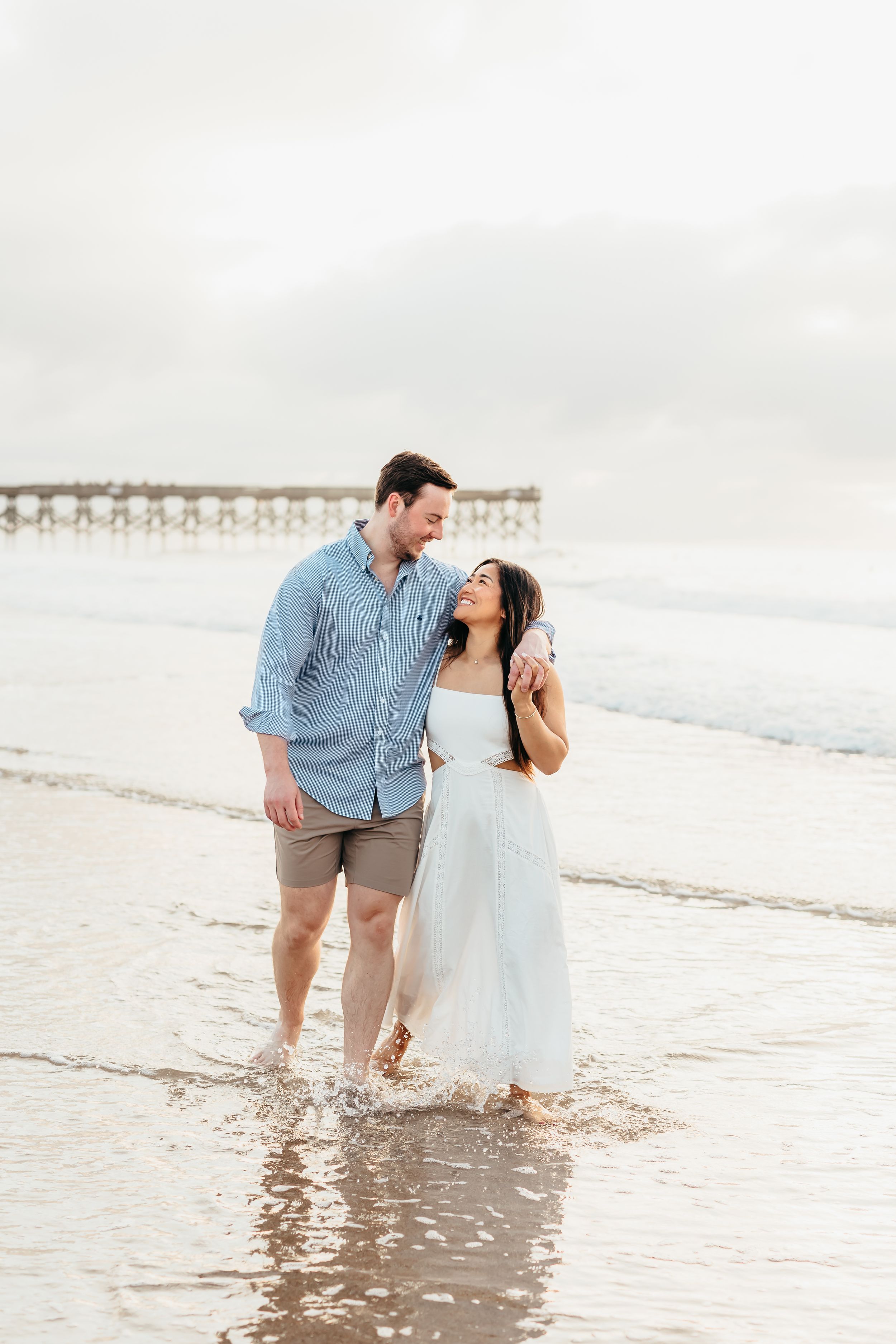 Playful couple splashes in ocean waves during beach photoshoot.
