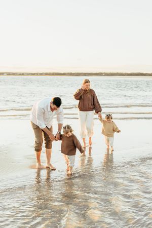 A family walks together in shallow ocean water at sunset on a peaceful beach.