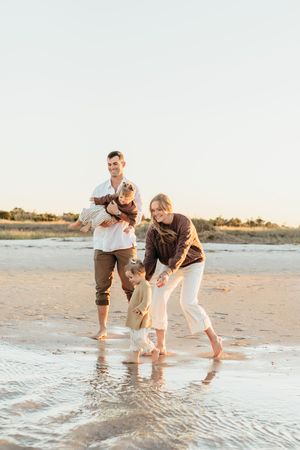 Family plays together at the beach during sunset, splashing in shallow ocean waves and enjoying quality time.
