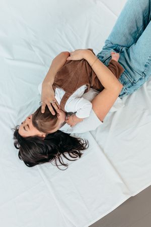 A person lies on white bedding while wearing a denim shirt and experiencing neck pain or discomfort.