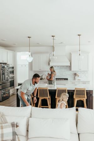 Family enjoying time together in a modern white kitchen with pendant lights and a dark island with wooden bar stools.