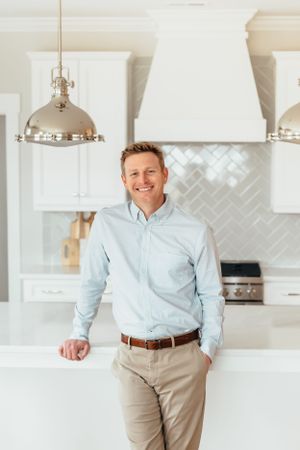 Professional portrait in a modern white kitchen with pendant lighting and herringbone tile backsplash.