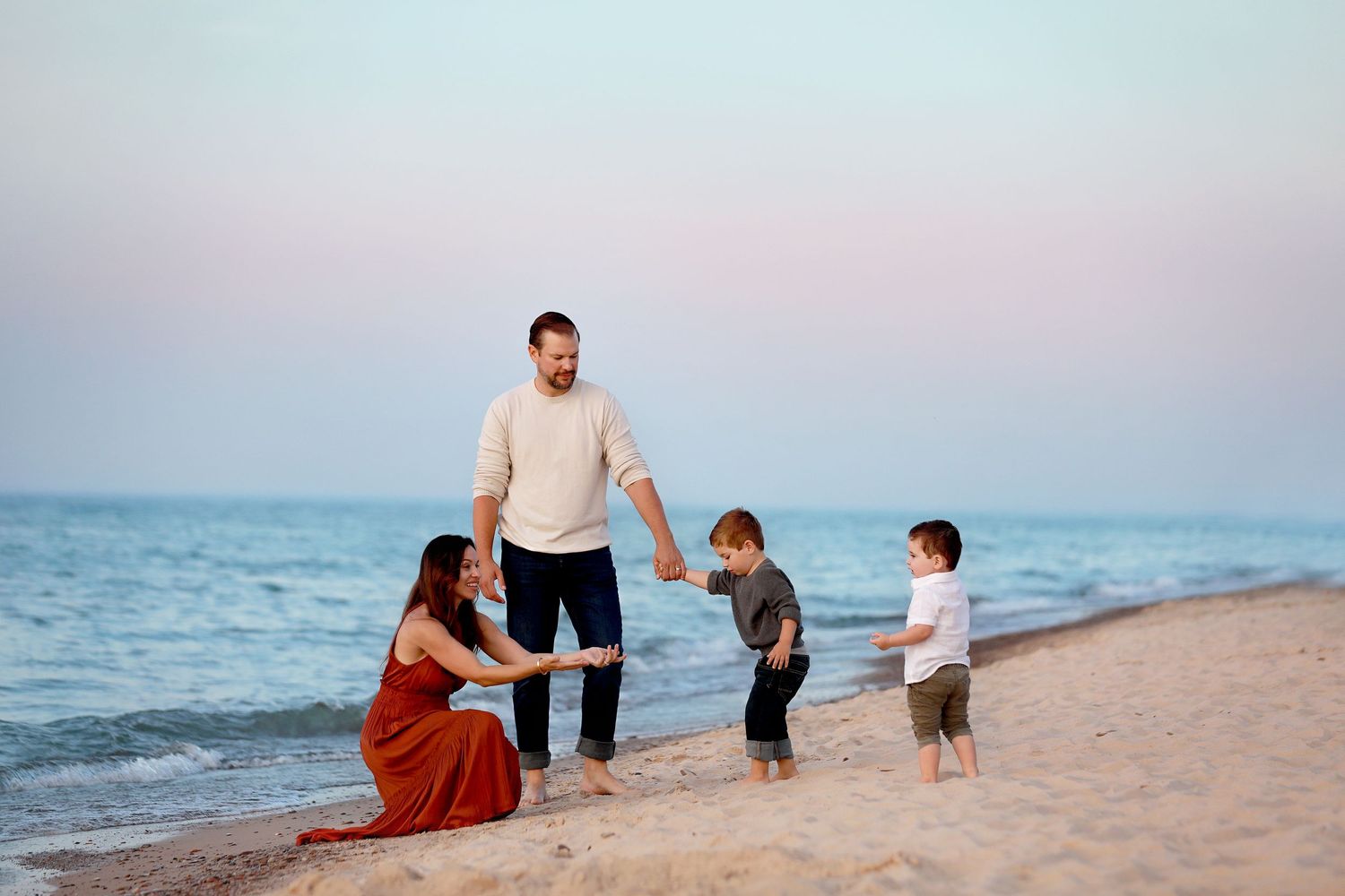 A family enjoys quality time together walking along a sandy beach at sunset with ocean waves in the background.