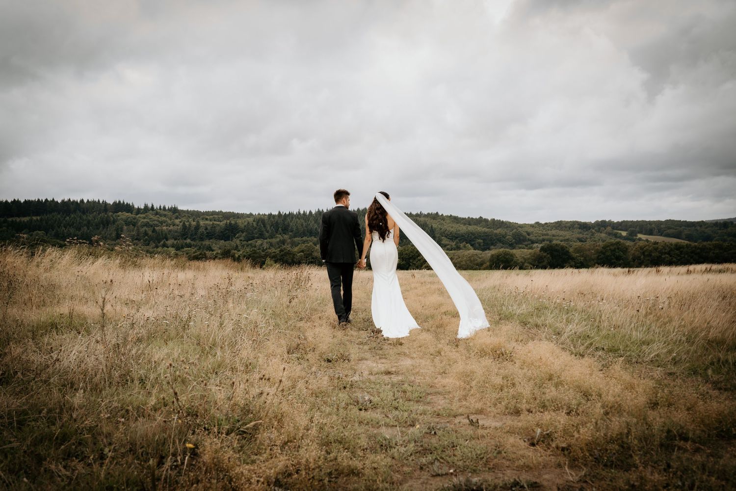 A newlywed couple walks together through a rural field at sunset in black and white.