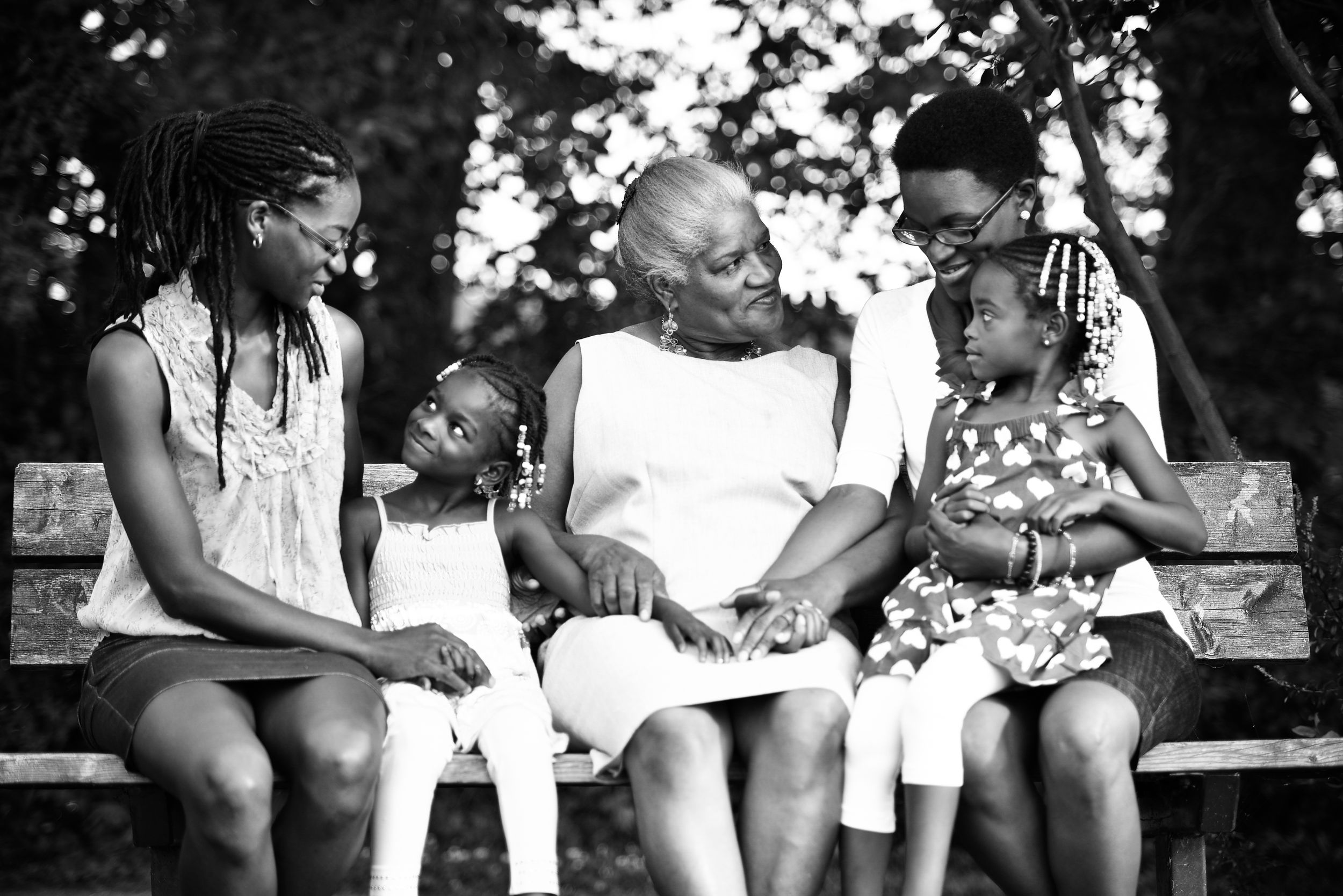 Black and white photo of multigenerational Black family sharing a warm moment together on a park bench.