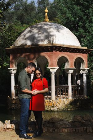 A domed gazebo with brick arches and white columns stands in a garden setting on a sunny day.
