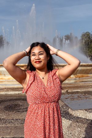 A joyful pose in front of water fountains wearing a red polka dot dress.