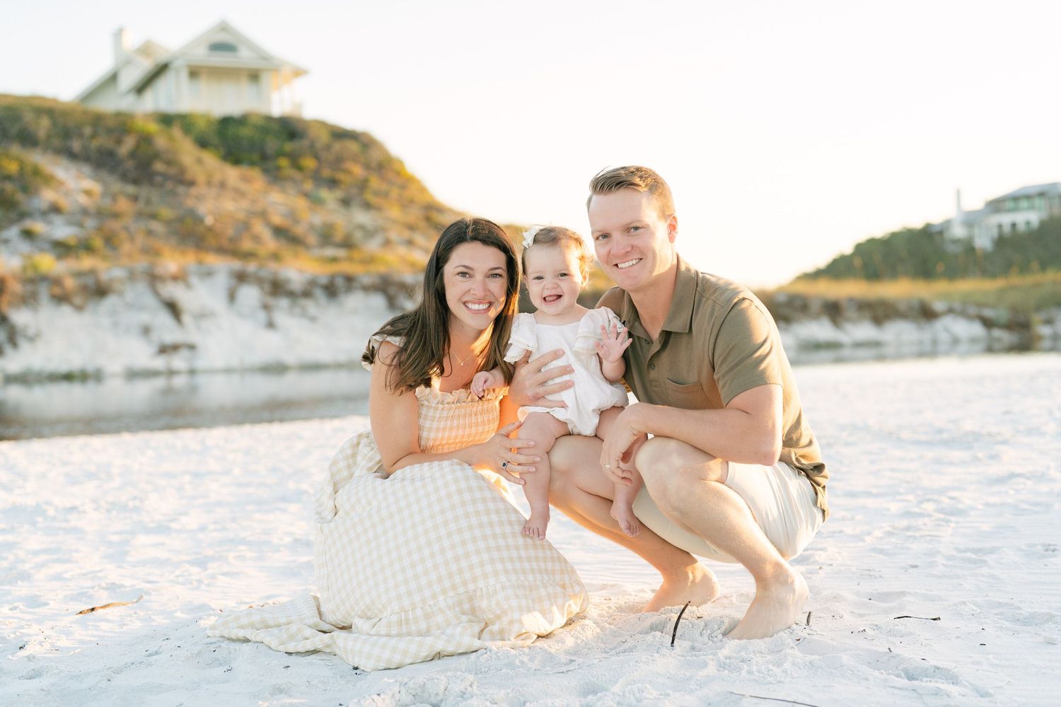 Family enjoying a sunset moment together on a white sandy beach with coastal homes visible in the background.