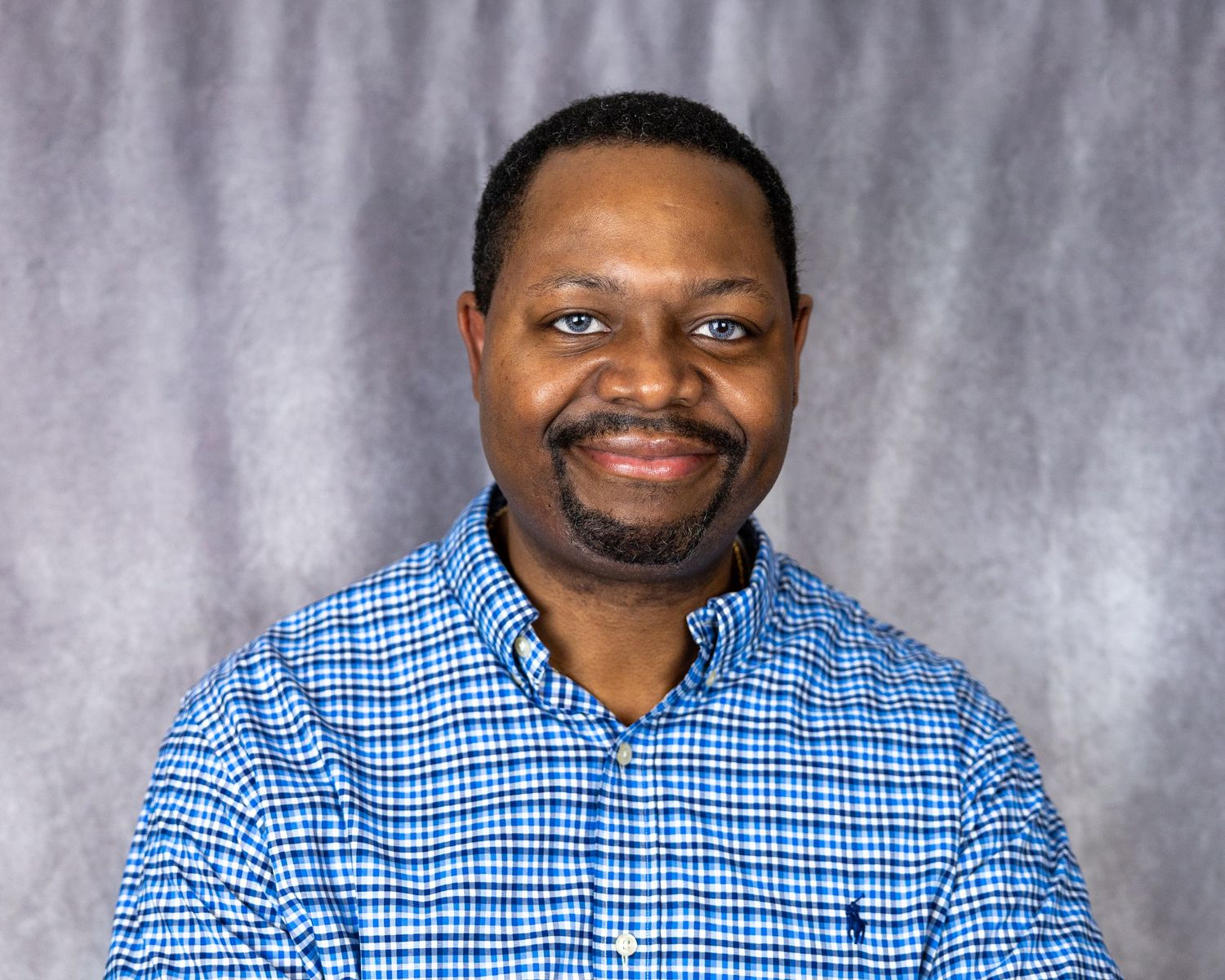 Portrait of a person wearing a blue checkered shirt against a gray backdrop.