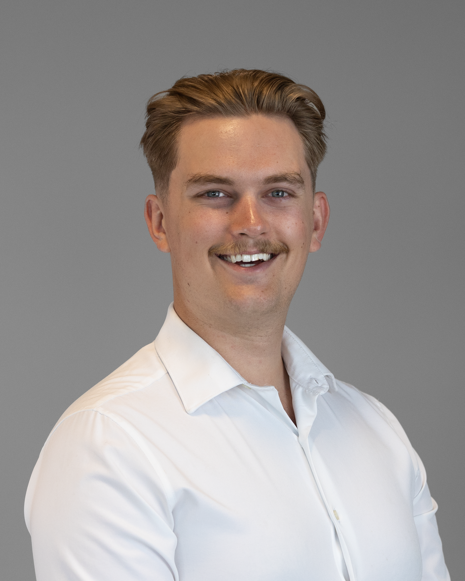 Professional headshot of a person wearing a white collared shirt against a gray background.