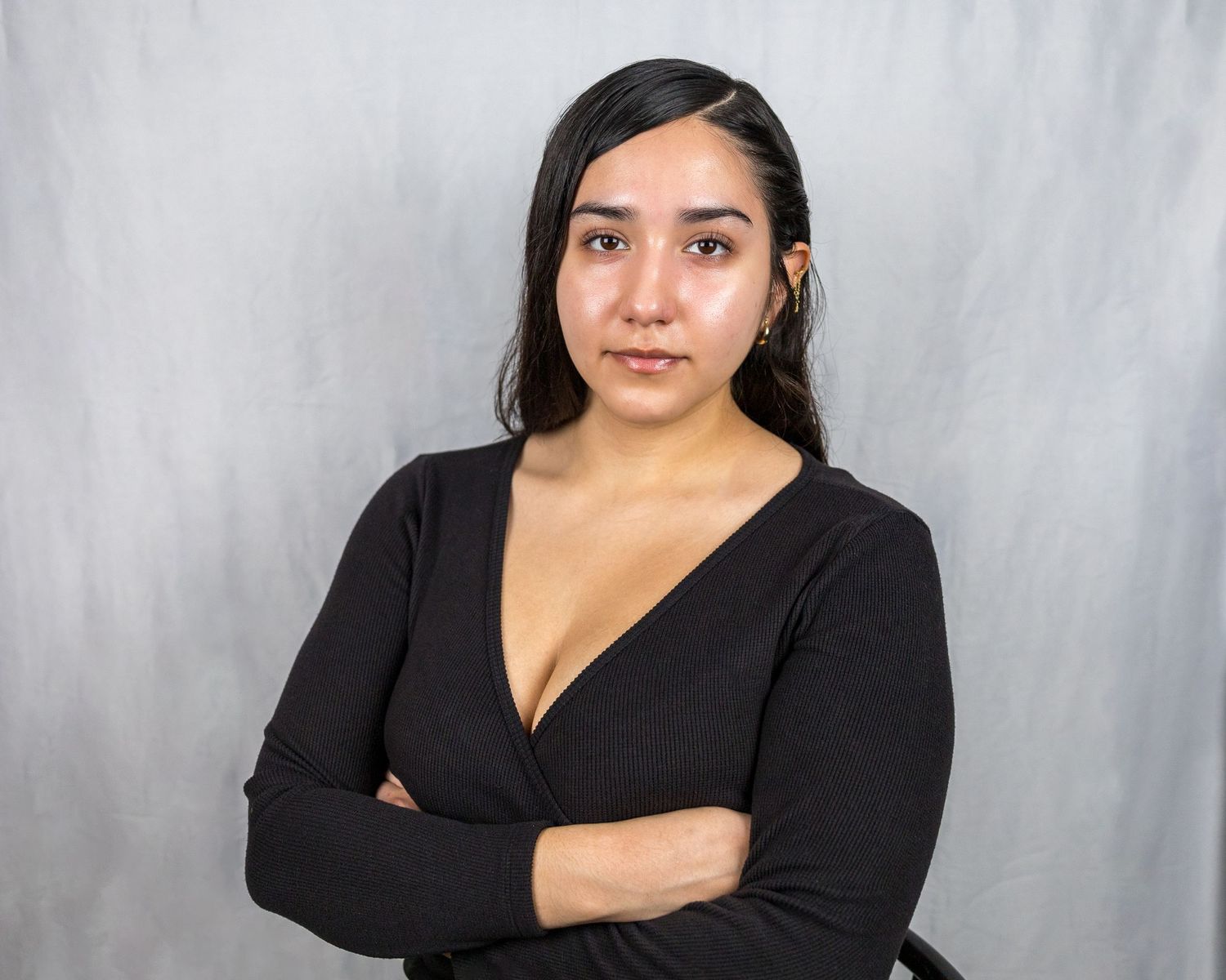 Portrait of a person in a black v-neck sweater against a gray background.
