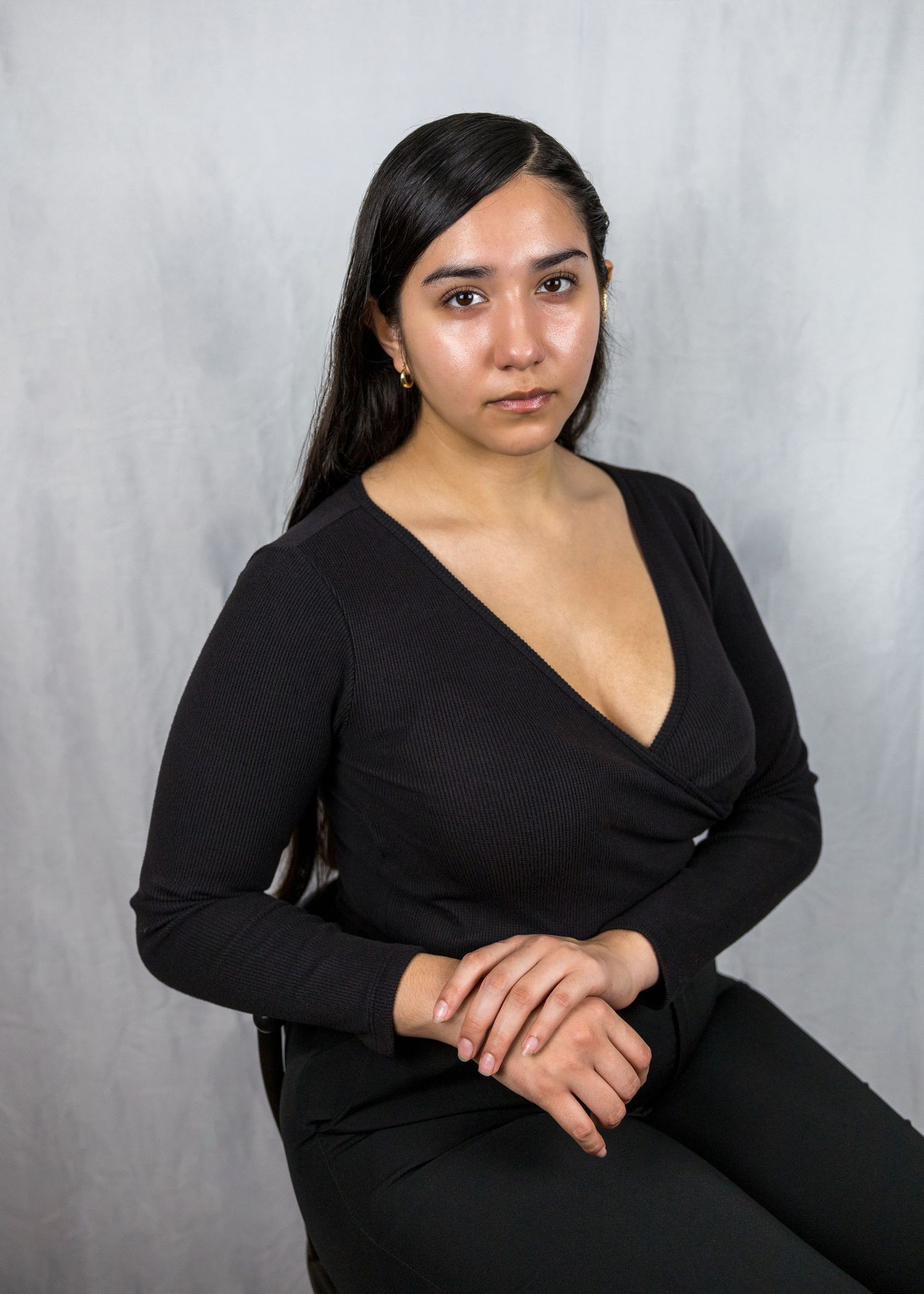 Studio portrait of a person wearing a black v-neck top against a gray backdrop.