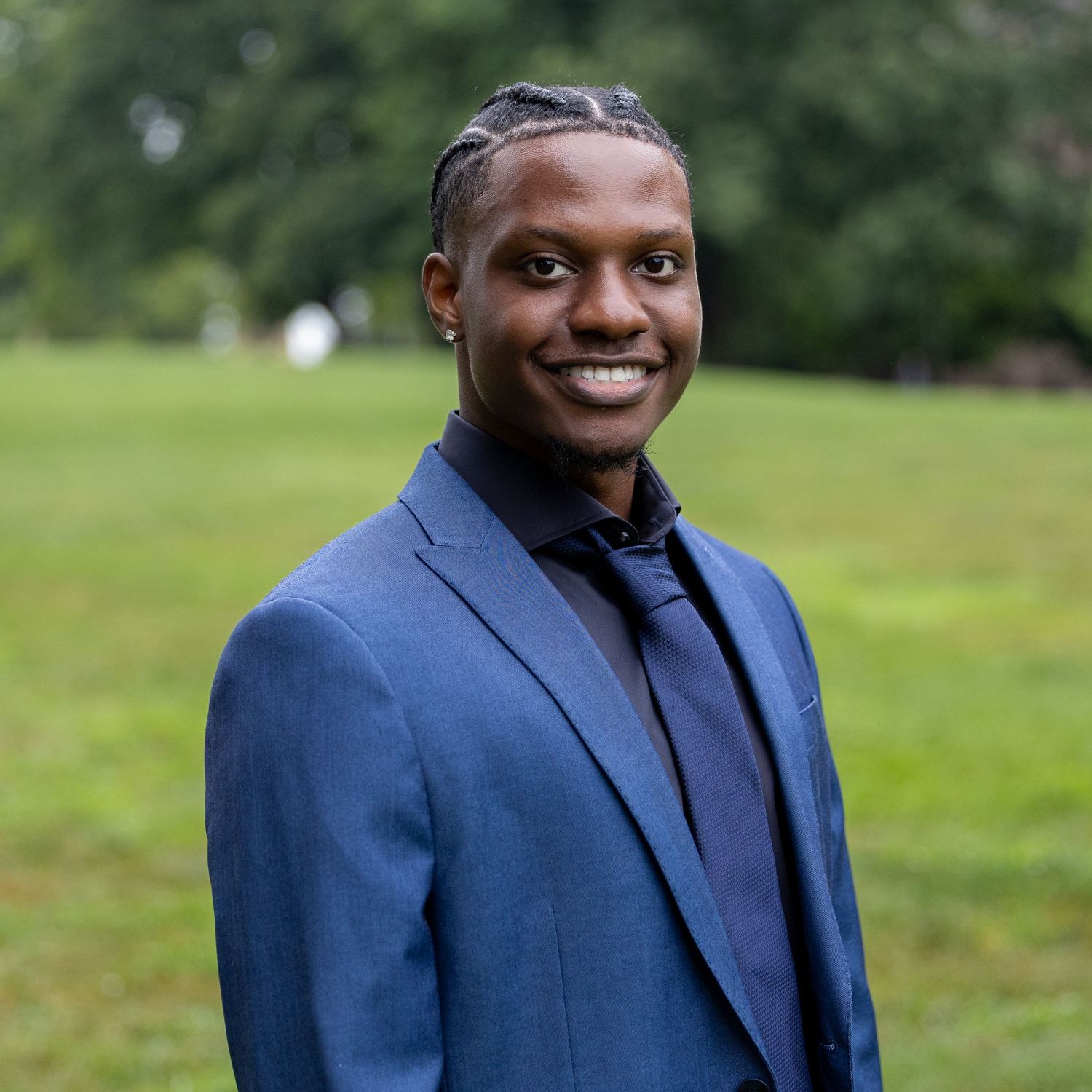 Professional headshot of person in blue blazer smiling against green background.