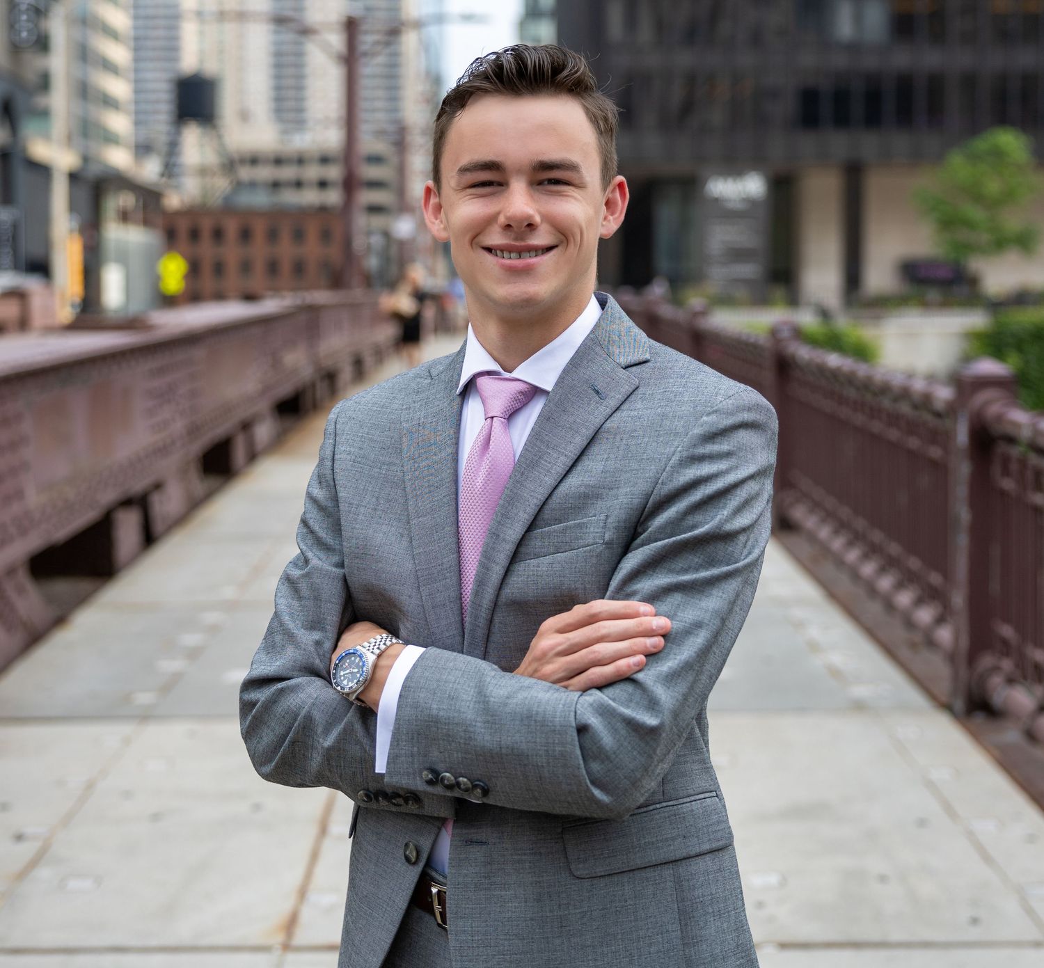 Business professional in gray suit and pink tie standing on urban bridge.