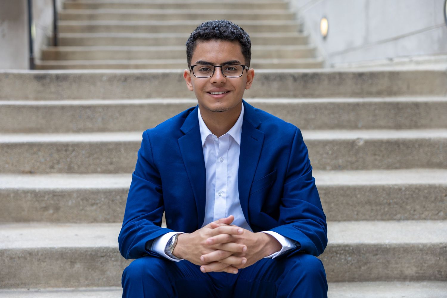 Professional in a blue blazer and white shirt sitting on concrete steps with a warm smile.