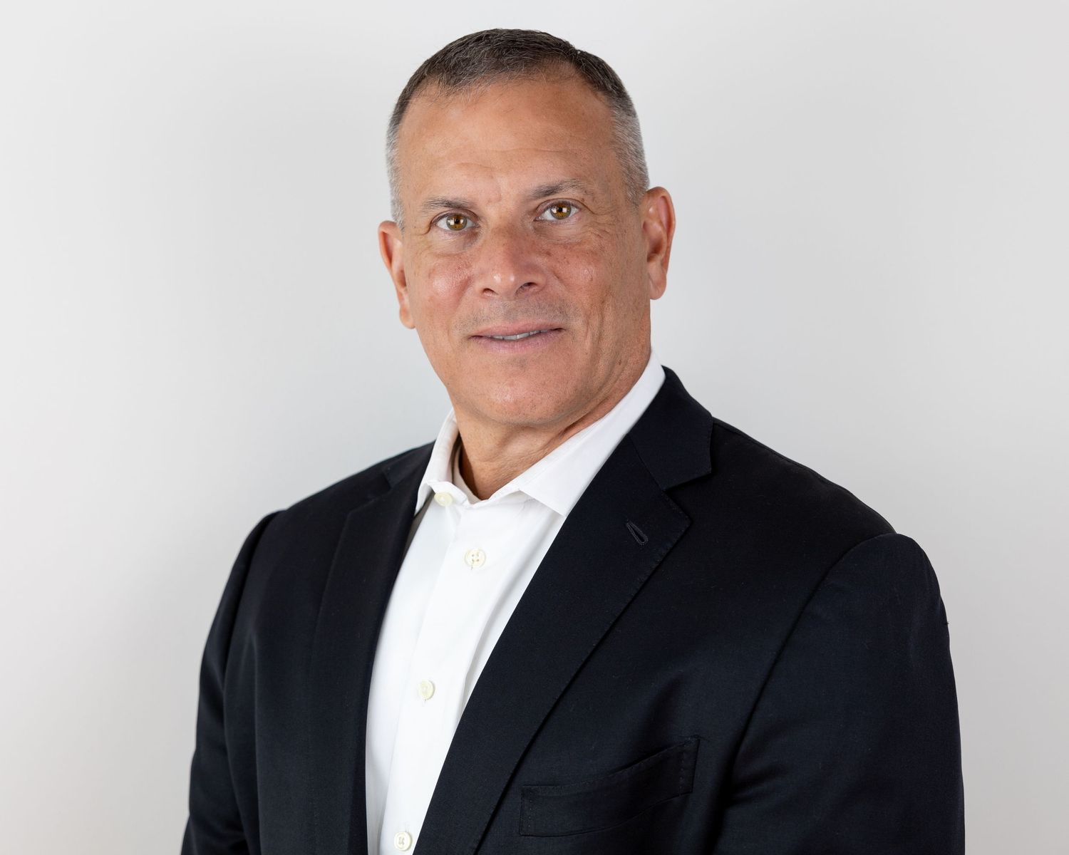 Business professional in dark suit jacket and white shirt against light background.