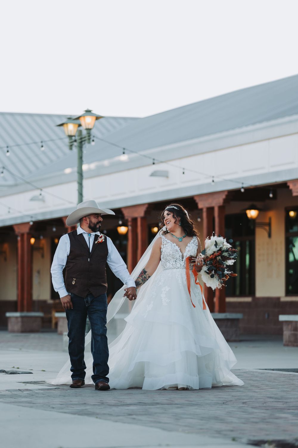 Wedding couple walking hand in hand outside venue at dusk.