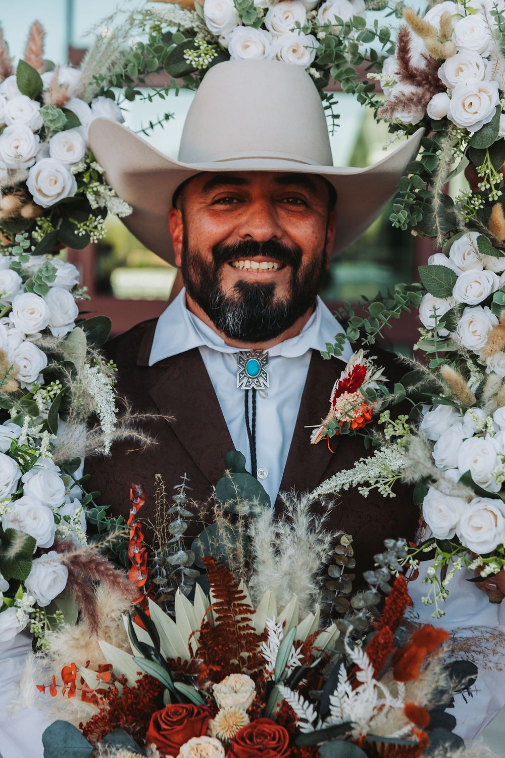 A floral arch decorated with white roses and rustic elements frames the wedding portrait.