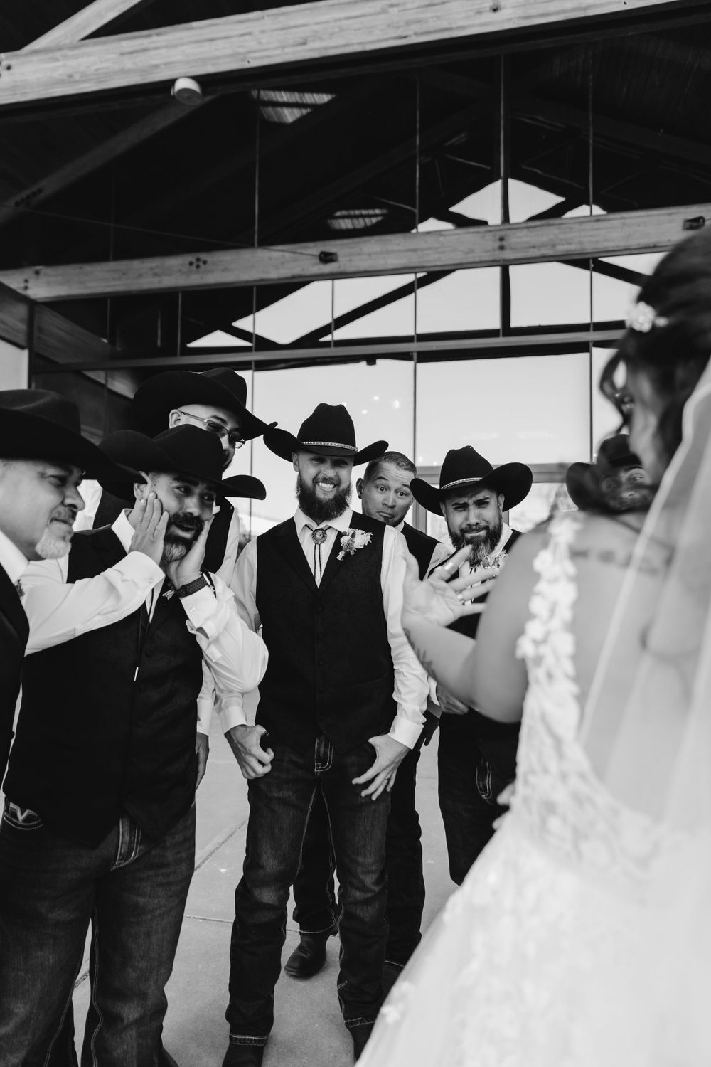 A black and white photo captures wedding guests in cowboy hats celebrating indoors.