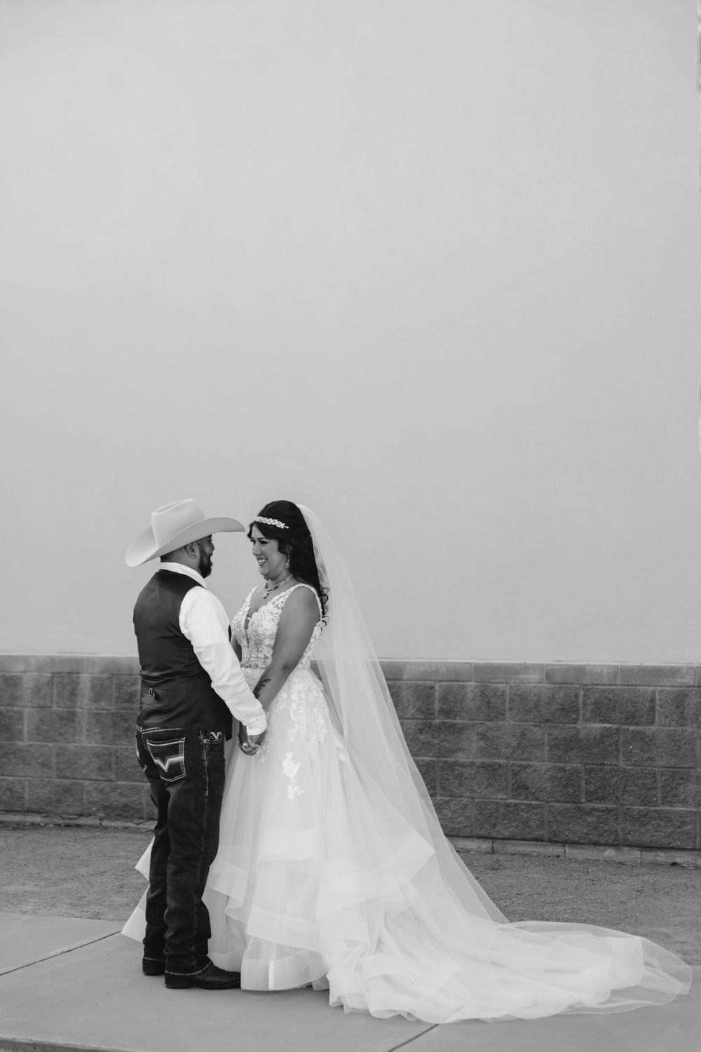 A romantic black and white wedding photo of a couple sharing an intimate moment against a stone wall.