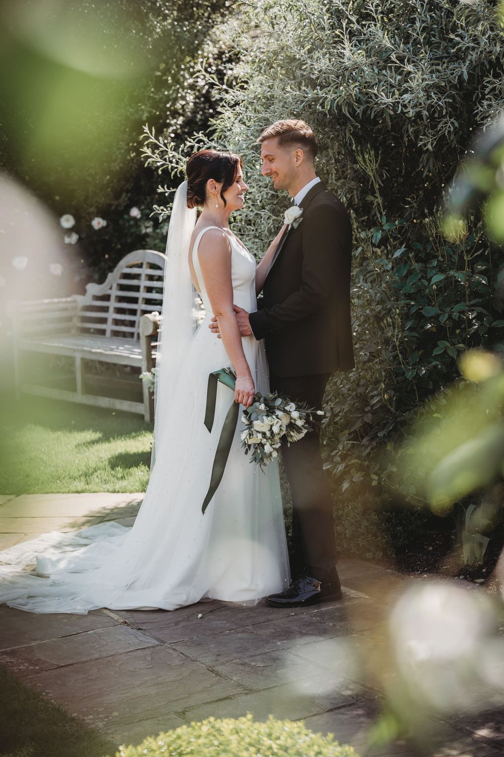 Newlyweds share romantic moment in garden setting with dreamy bokeh effects.