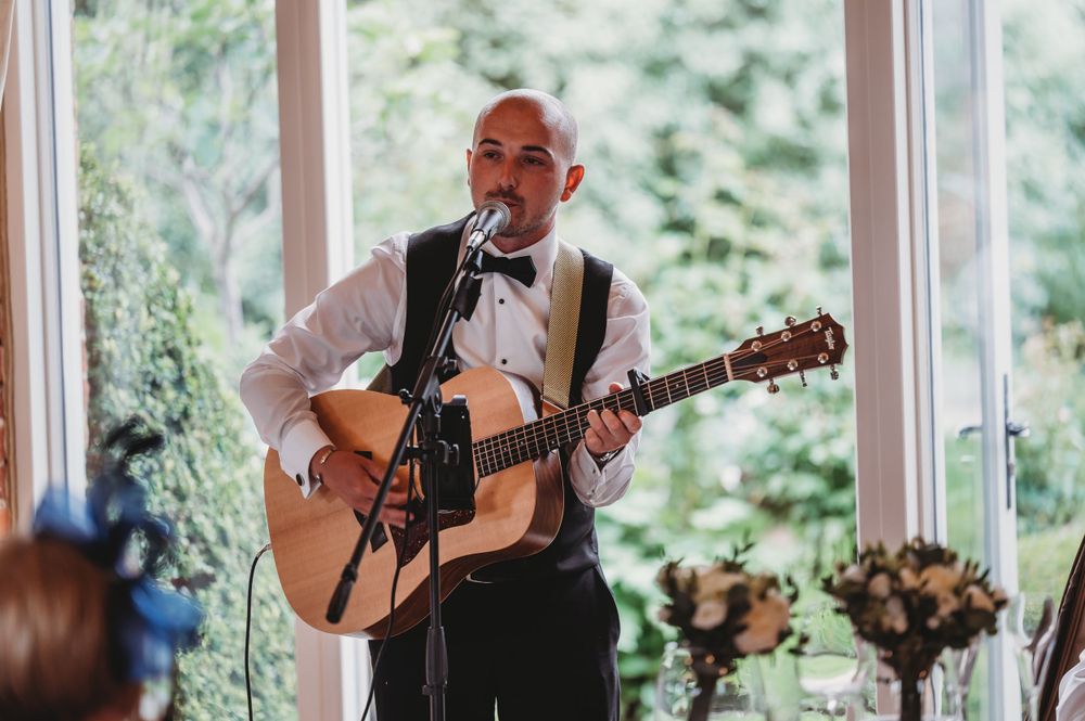 Musician performs with acoustic guitar during wedding reception in sunlit venue.