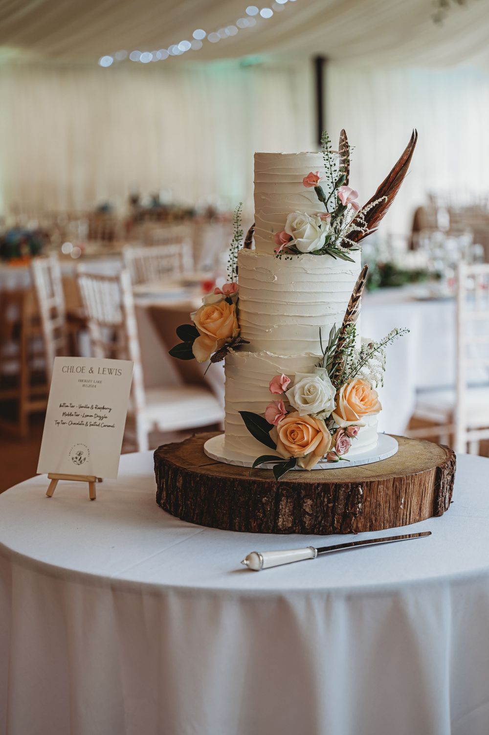 Elegant three-tier wedding cake decorated with peach and white flowers on wooden stand.