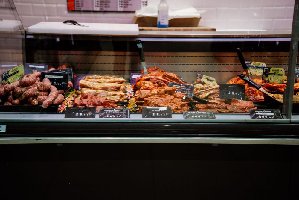 A refrigerated deli case displaying an assortment of fresh meats and charcuterie with price labels.