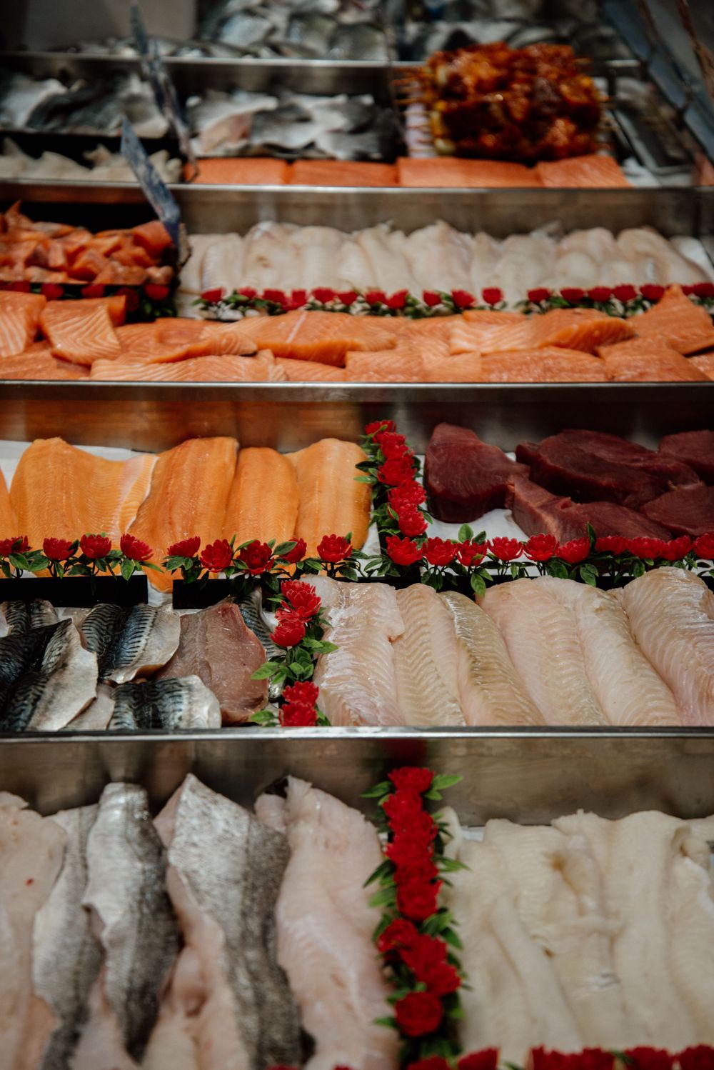 A fresh fish market display with rows of salmon, white fish fillets, and tuna decorated with red flowers.