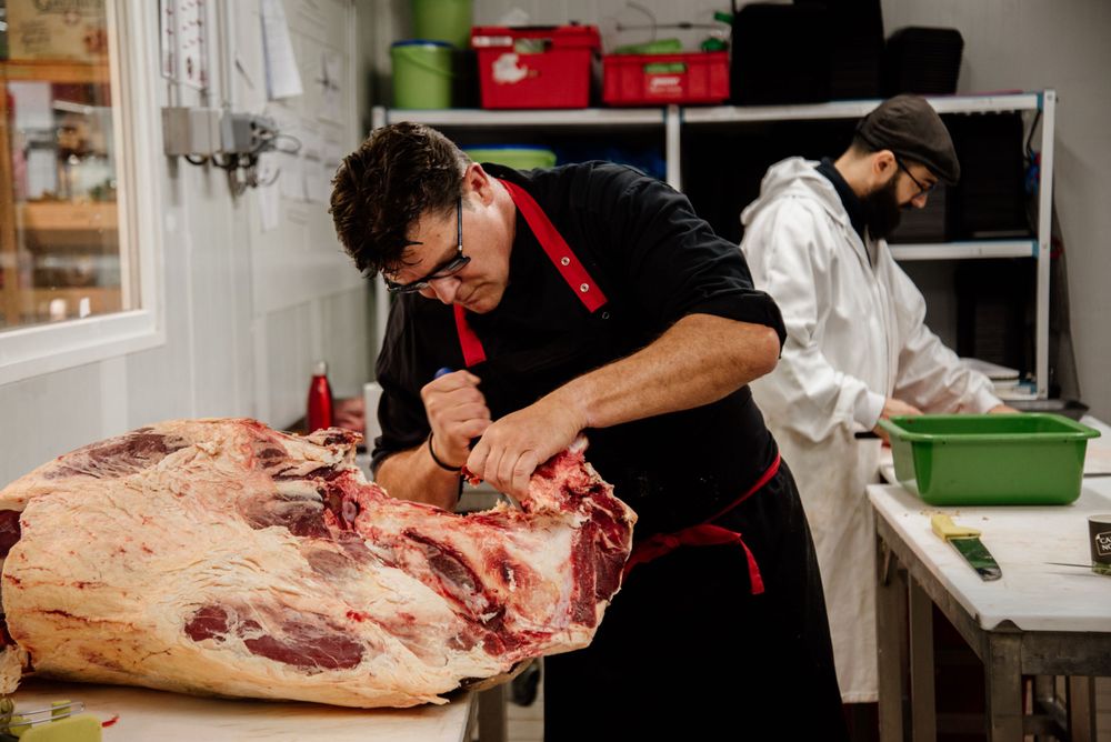 Professional butcher in black apron skillfully breaking down a large cut of beef in a meat shop.