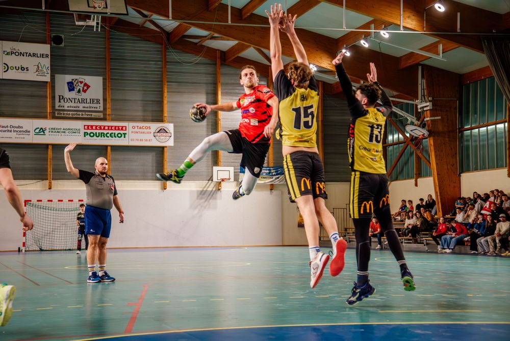 Athletes jumping during an intense indoor handball game with spectators watching in the background.