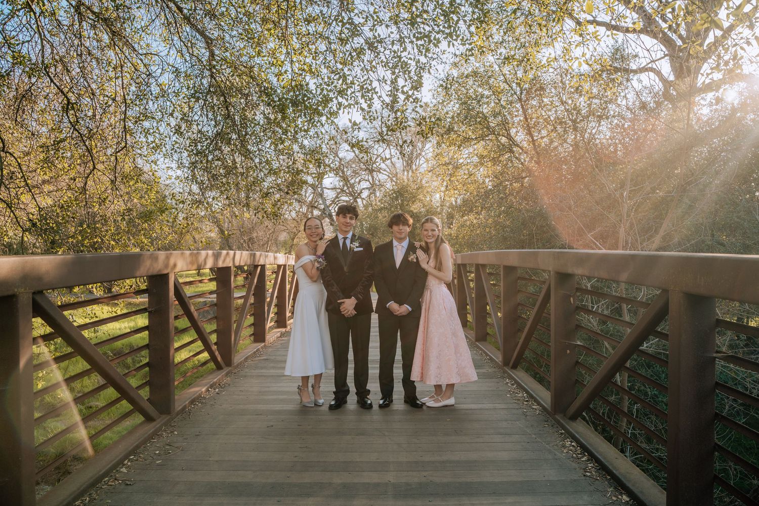 Wedding party standing together on wooden bridge in natural setting.