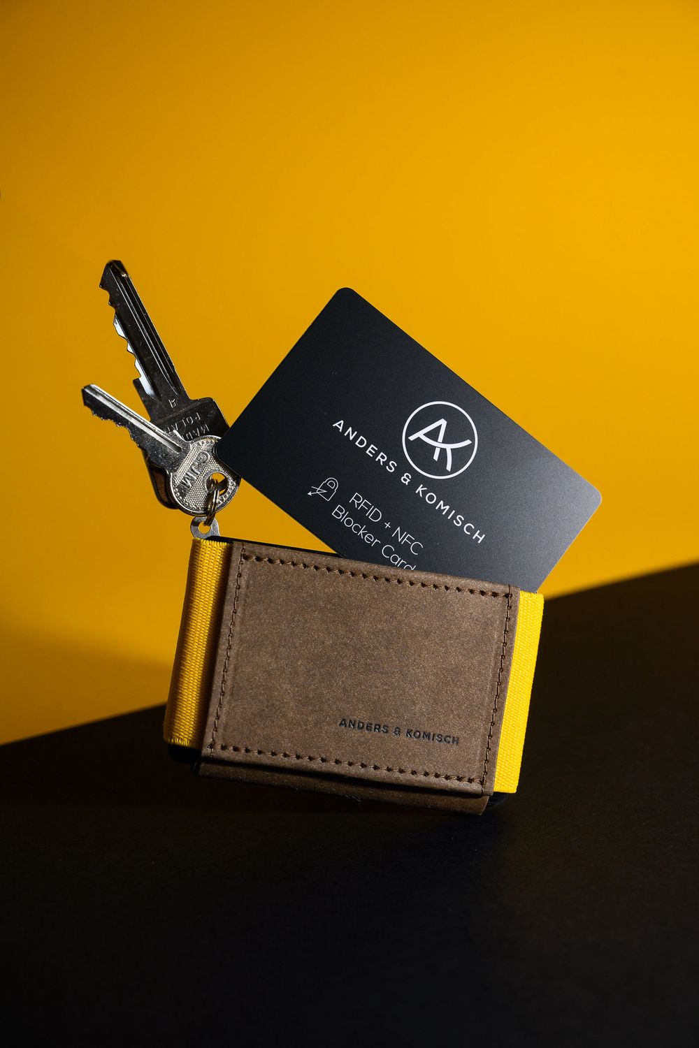 Brown leather wallet with keys and black membership card on yellow and black background.