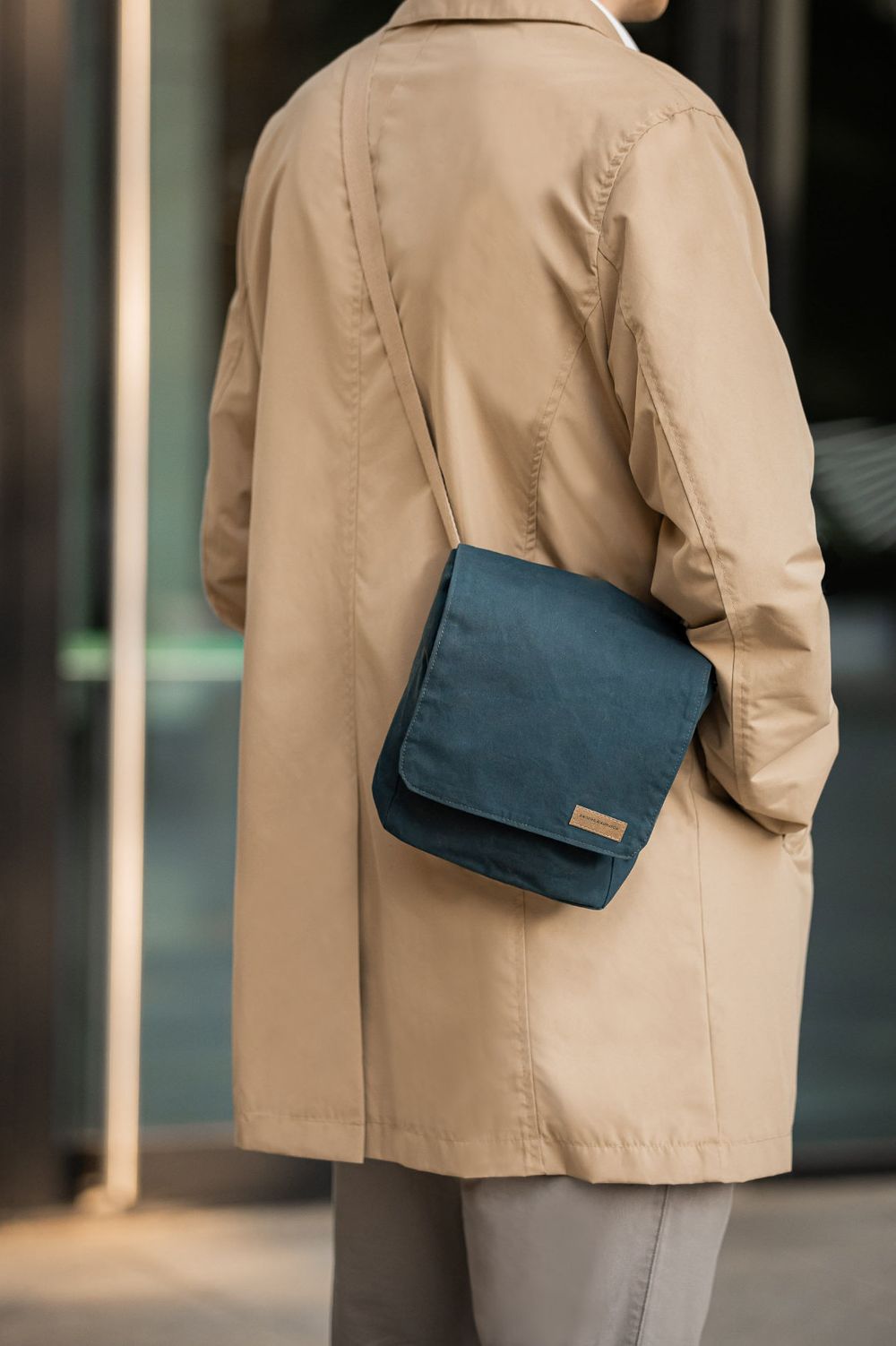 Navy messenger bag worn with beige trench coat in urban setting.