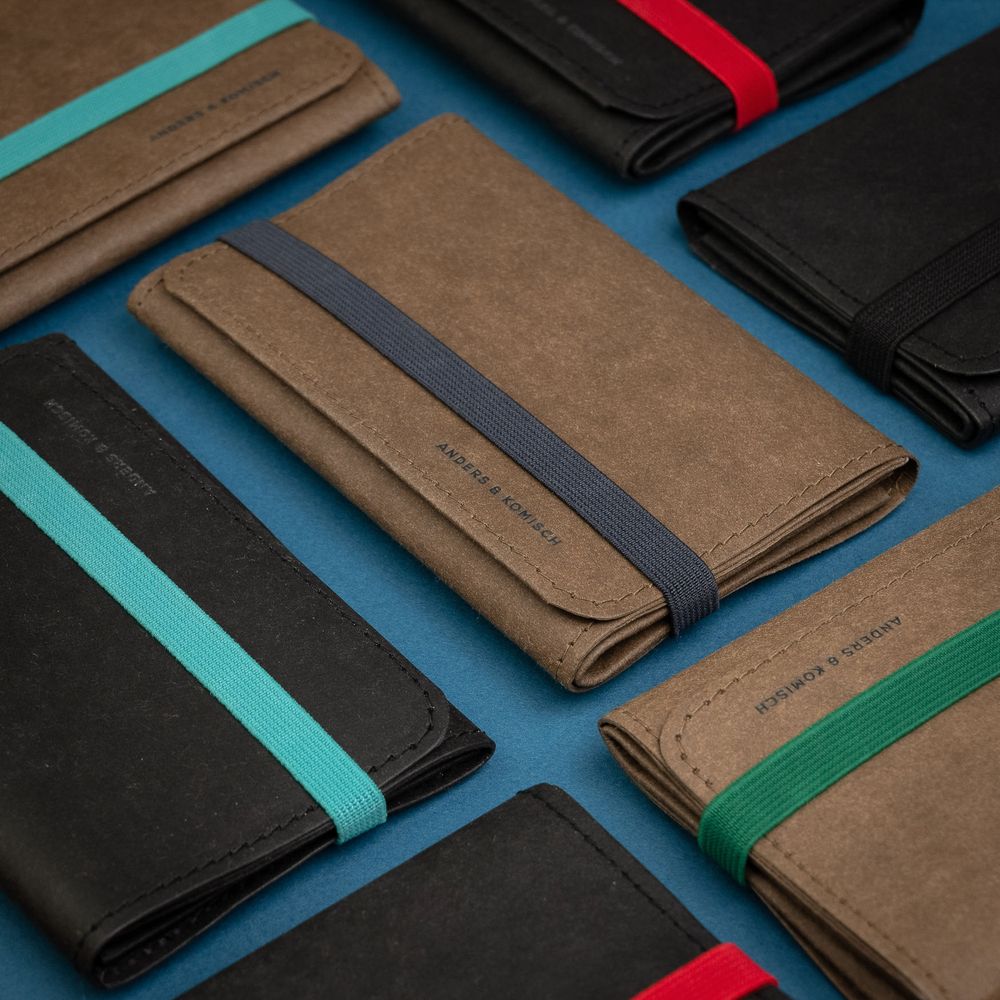 Collection of minimalist wallets in brown and black with colorful elastic bands laid out on blue surface.