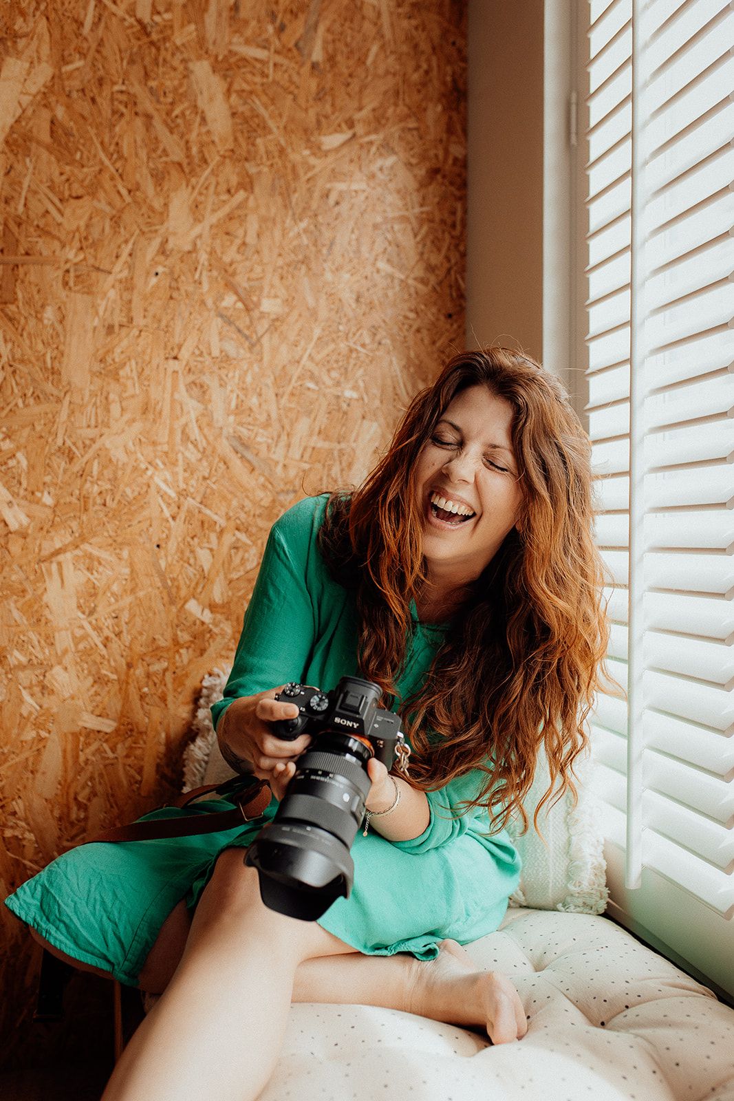 Photographer in green shirt lying down with camera taking creative self portraits by window with natural light.