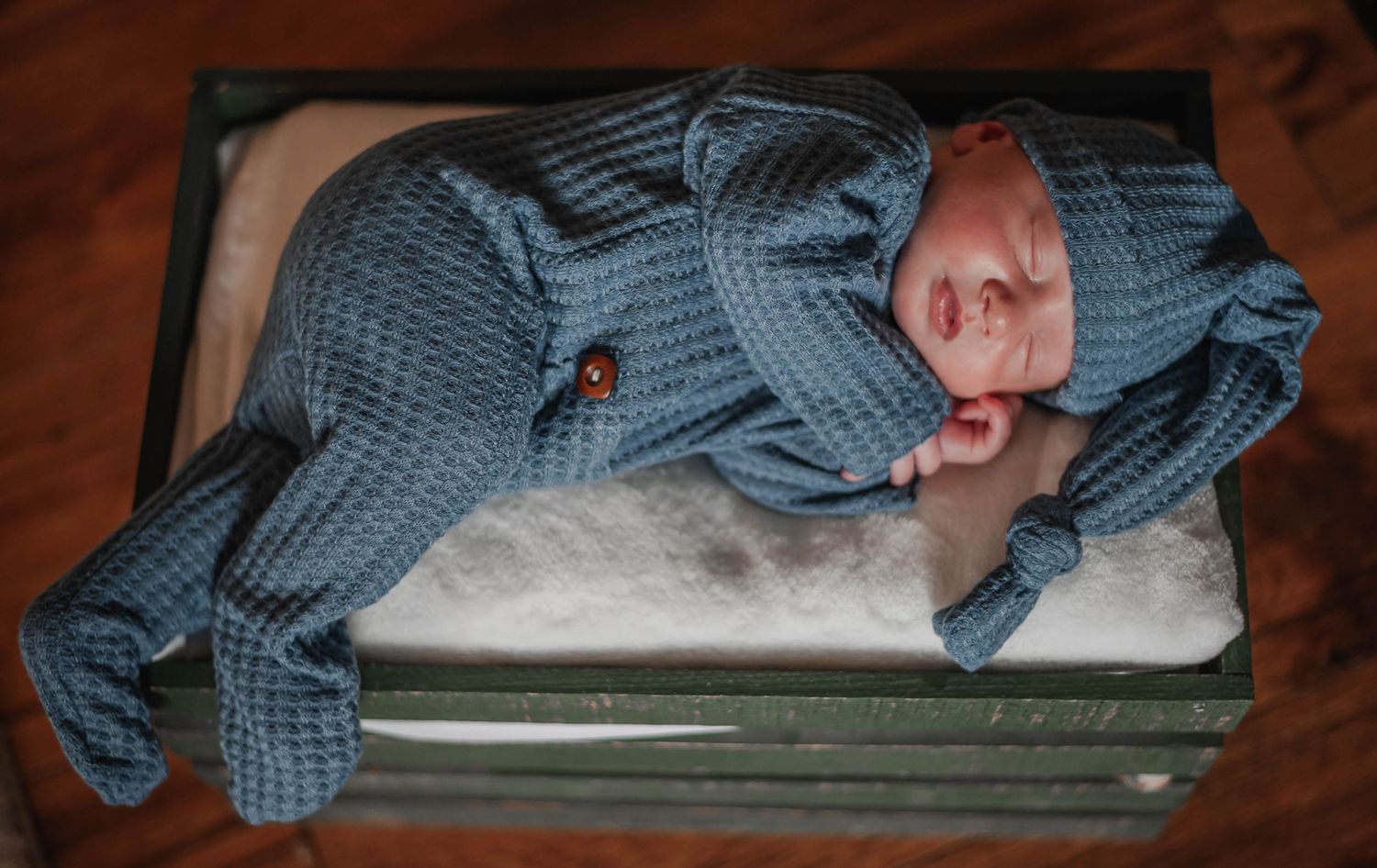Newborn in blue knit outfit sleeping on white fabric.