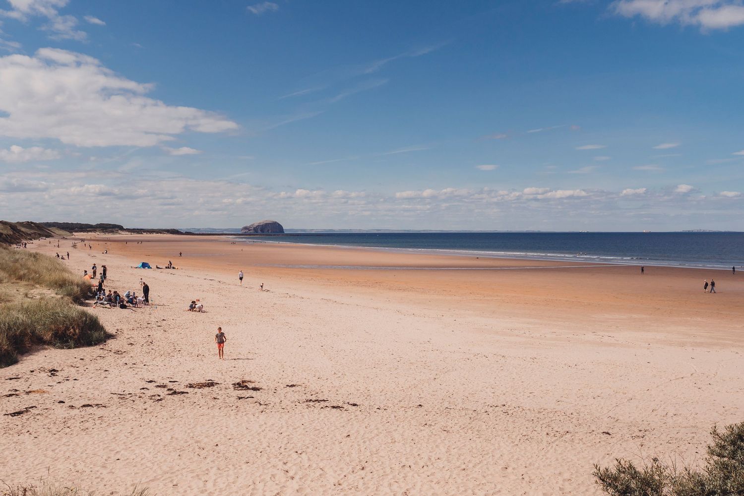 Wide sandy beach with scattered beachgoers and coastal cliffs in the distance.