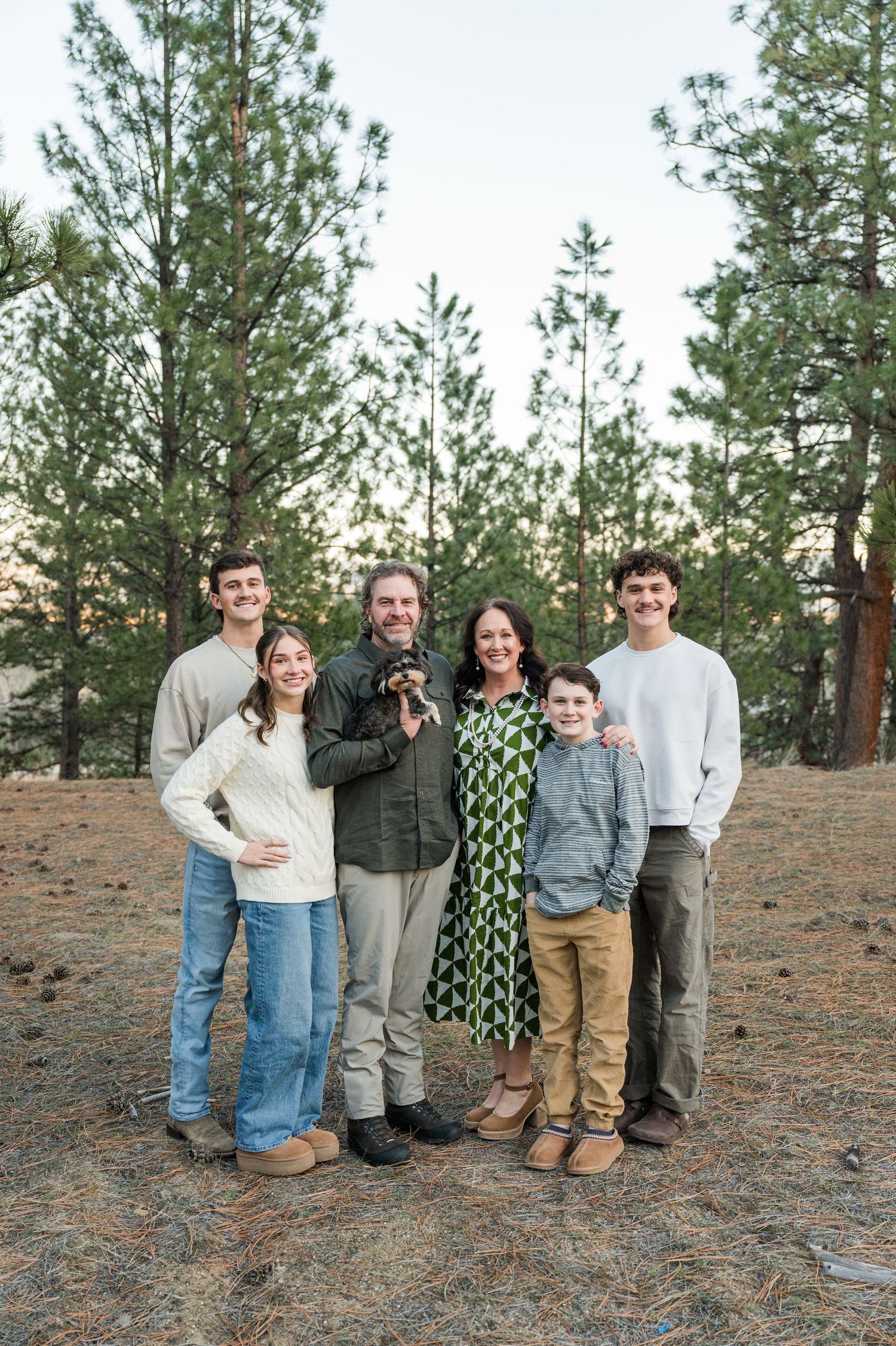 Family group poses together among tall pine trees in a forest setting.